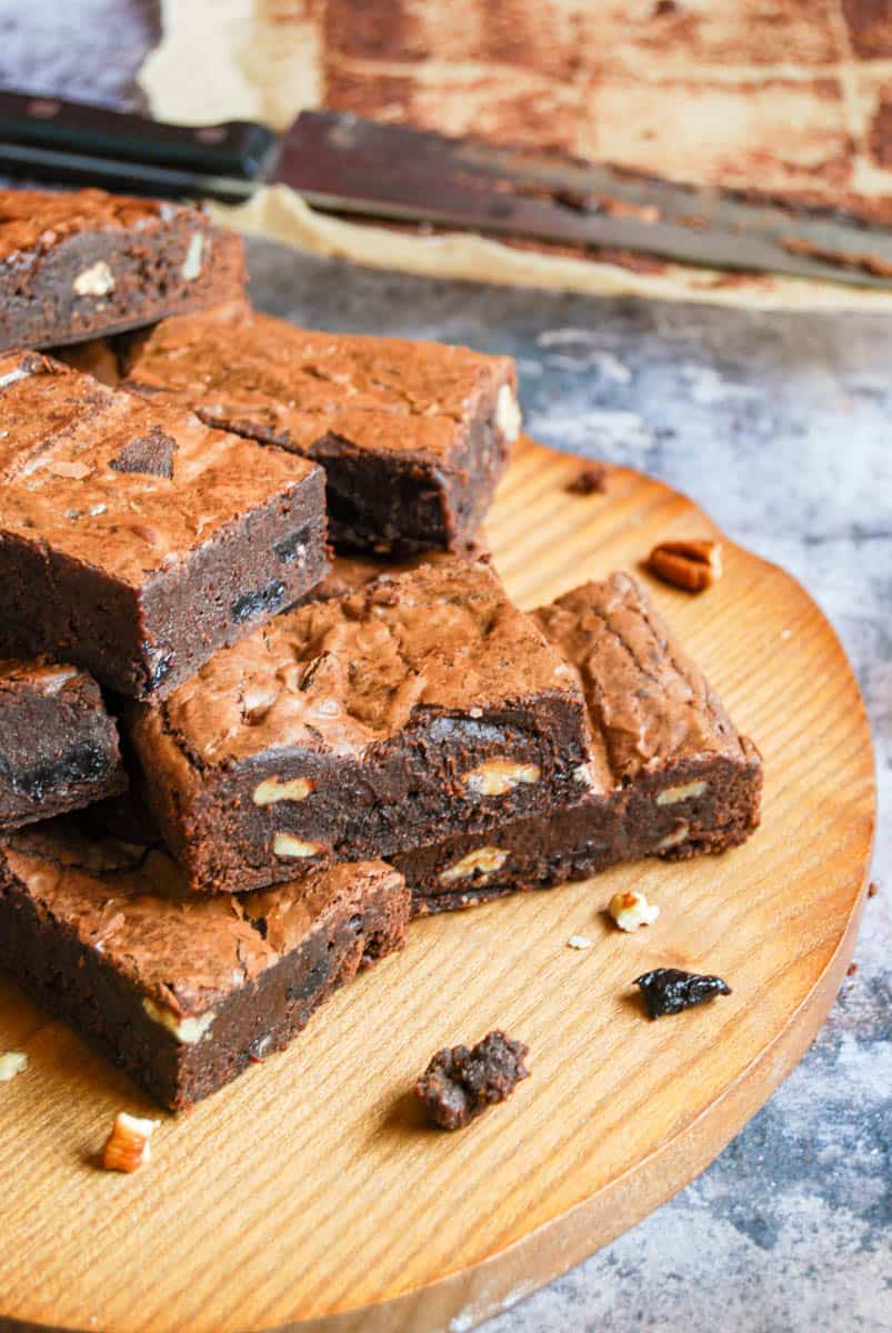 A batch of chocolate brownies with dried cherries and pecan nuts on a wooden board.