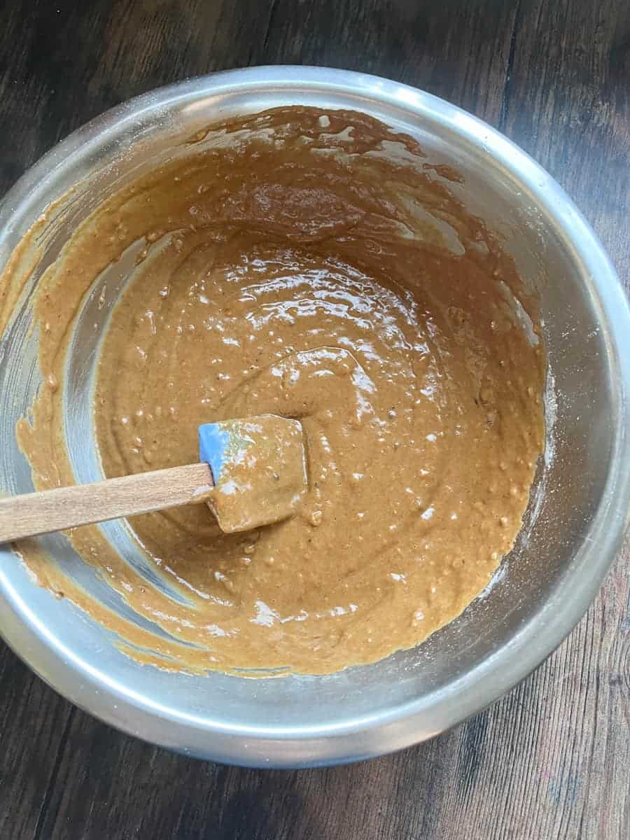 A silver bowl of pumpkin cake batter with a wooden spatula.