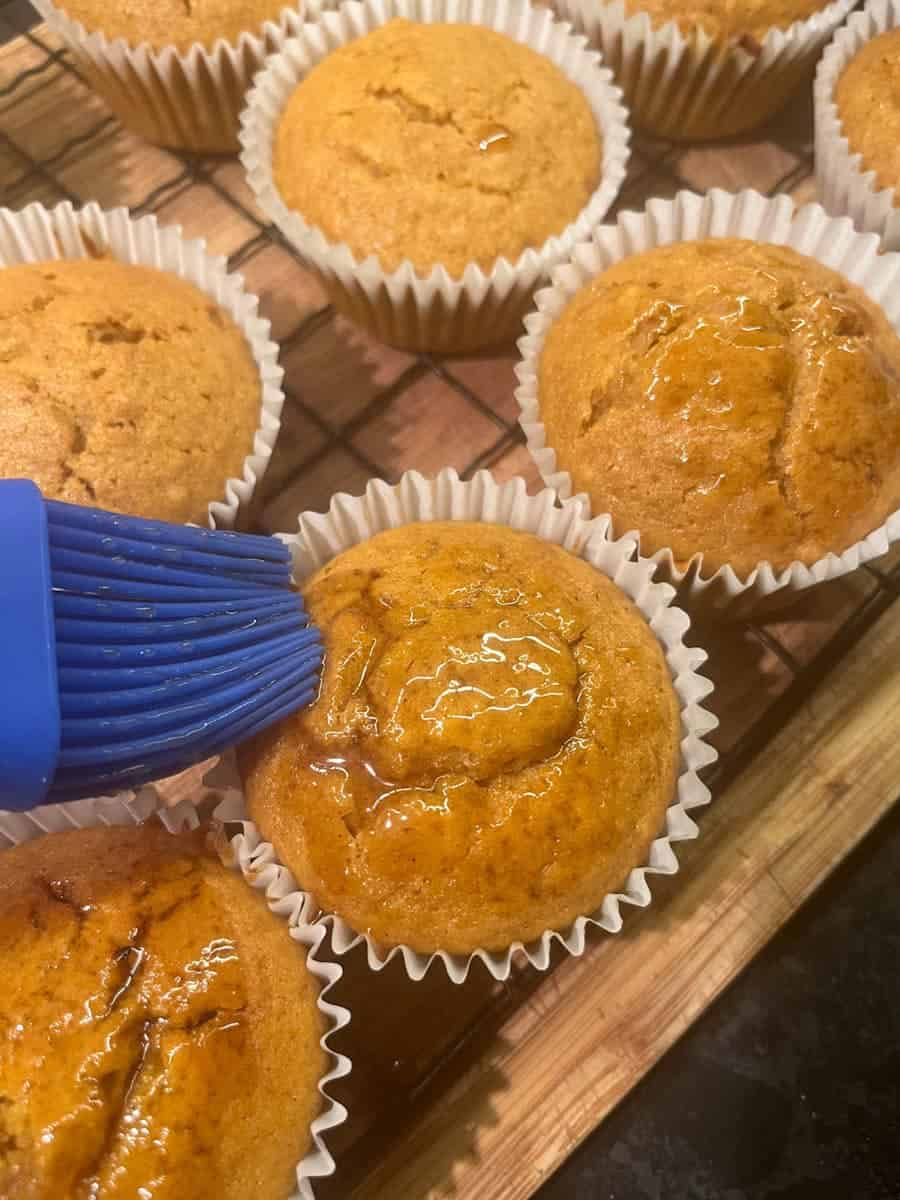 Coffee syrup being brushed onto pumpkin cupcakes with a blue pastry brush.