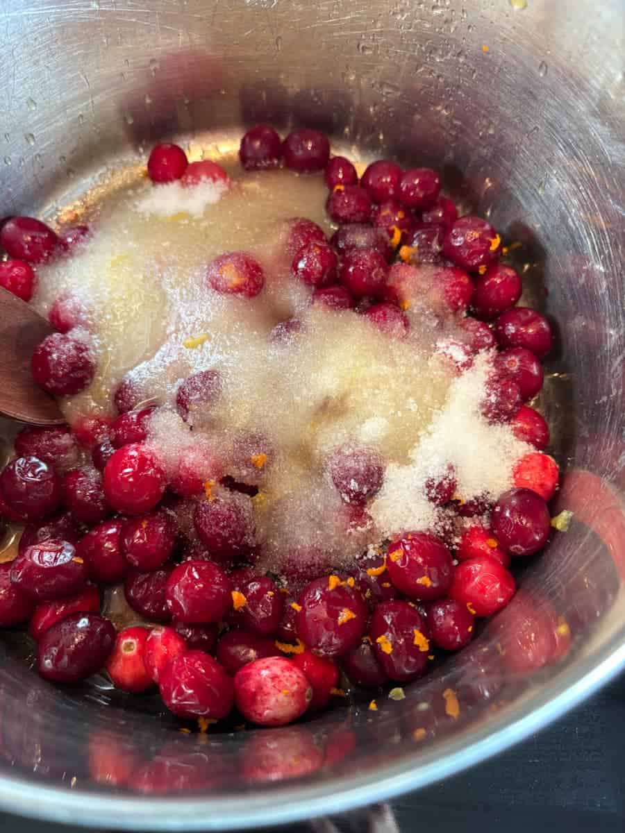 Fresh cranberries, white sugar and grated orange zest in a silver saucepan.