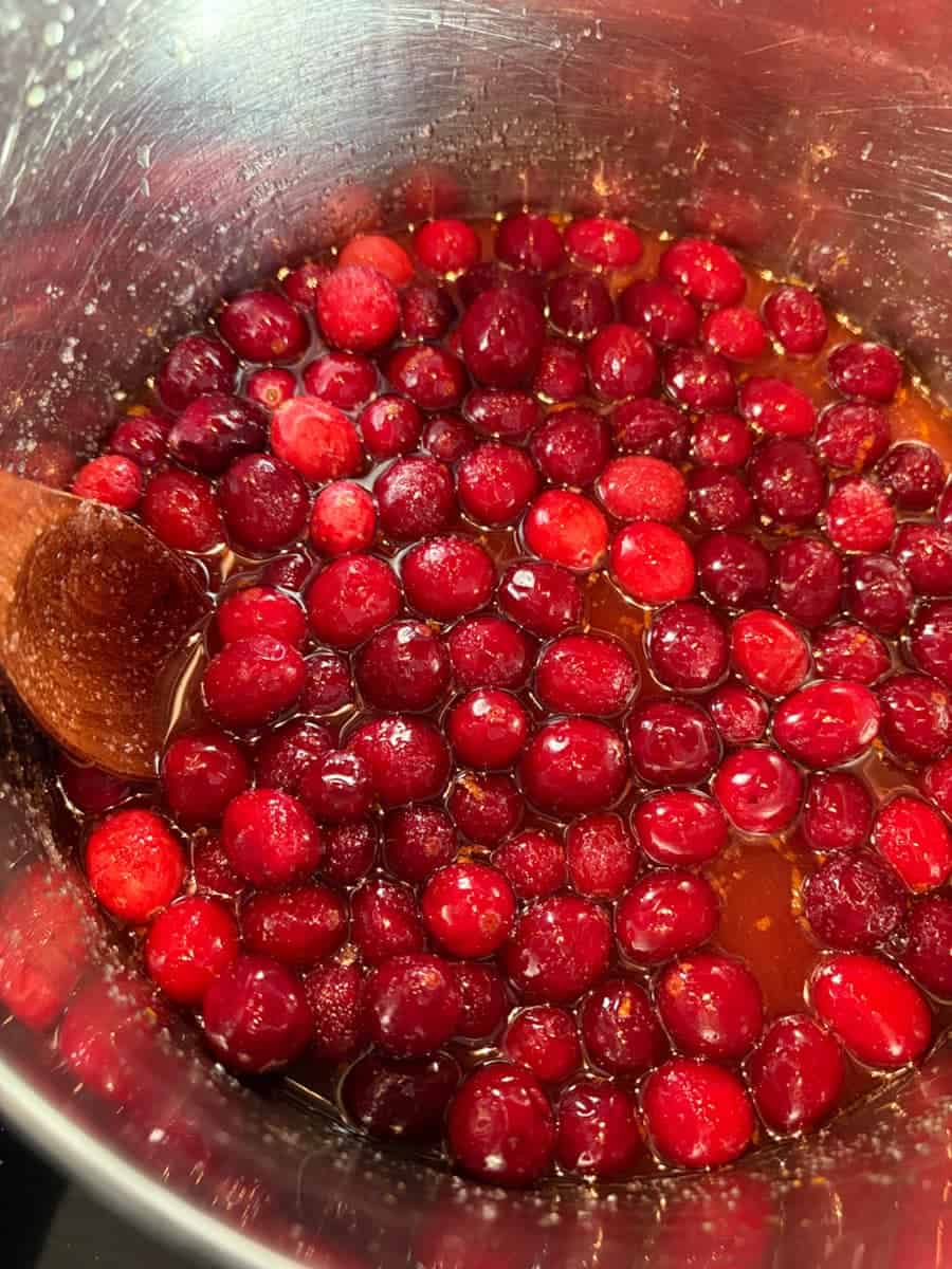 Fresh cranberries and orange juice in a silver saucepan with a wooden spoon.