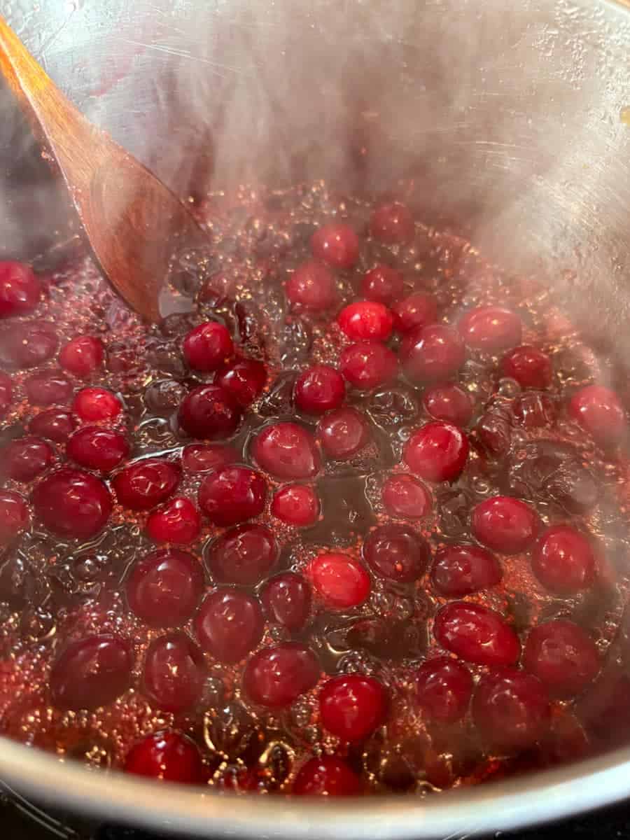 Fresh cranberries simmering in sugar and orange juice in a silver pan to make cranberry sauce.