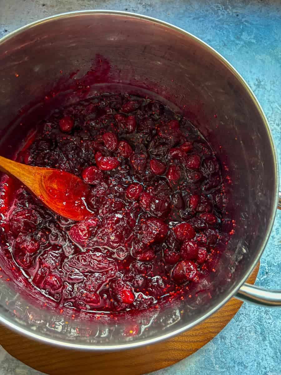 A silver saucepan of cranberry sauce with a wooden spoon.