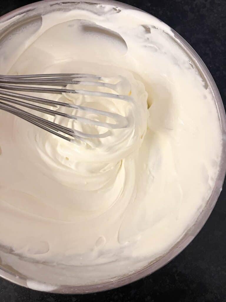 A silver bowl of whipped cream and a silver whisk.