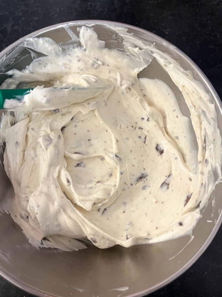 A silver bowl of no bake cheesecake mixture with grated chocolate.