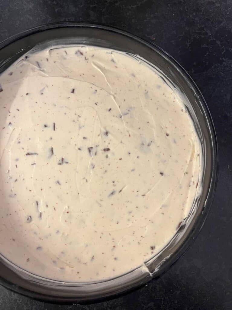 A no bake cheesecake with grated chocolate in a black round baking tin.