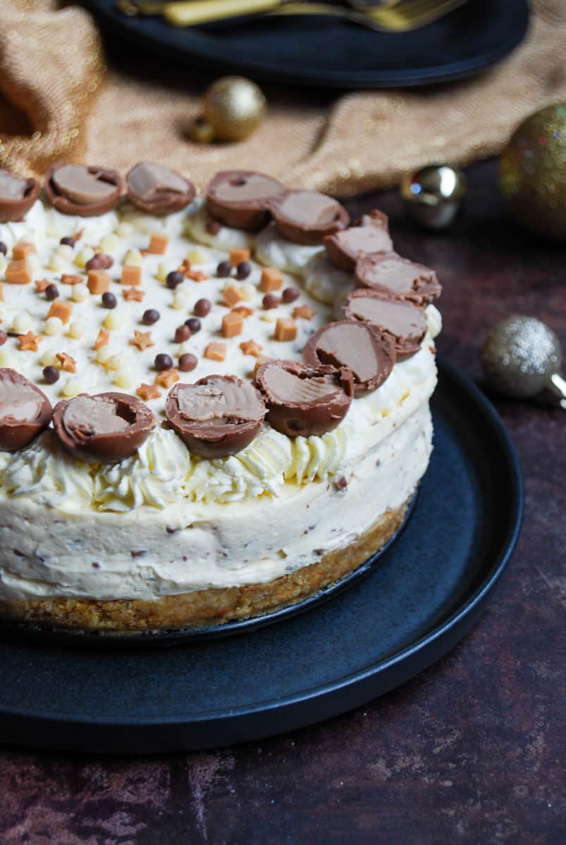 A Baileys cheesecake decorated with whipped cream, chocolate truffles, gold stars and small fudge pieces on a black plate.