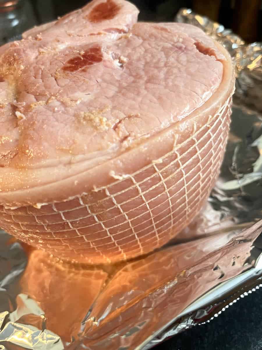 A cooked ham with string to secure it on a foil lined tin.