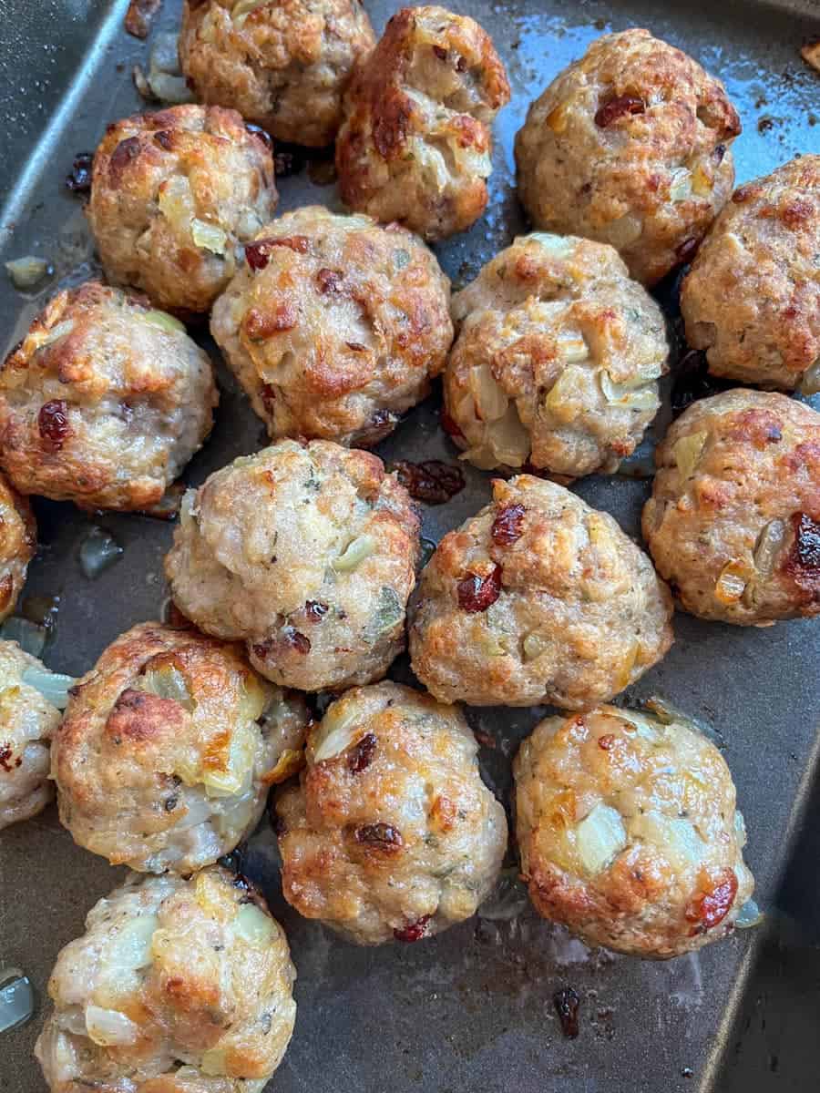 Sausage stuffing balls with chopped sage and dried cranberries on a baking sheet.