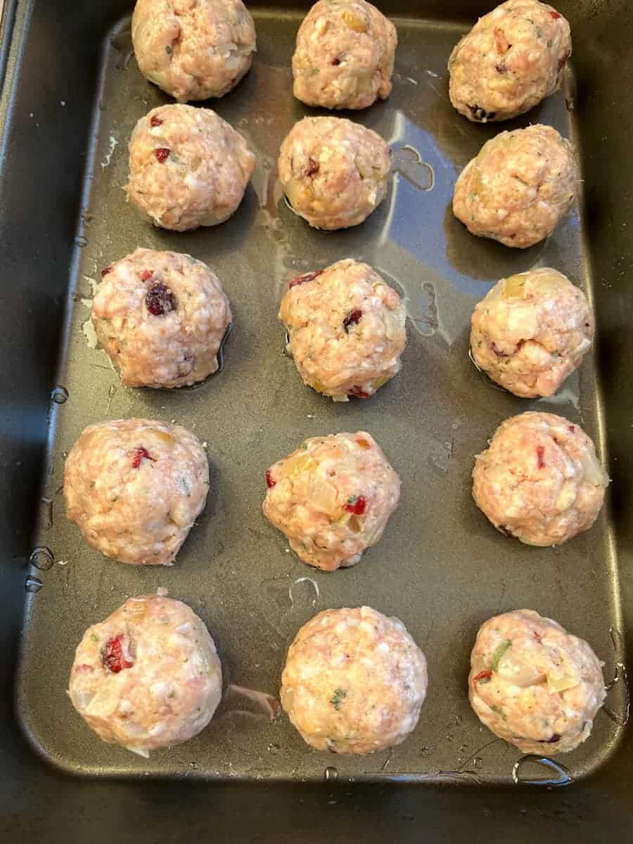 15 uncooked sausage stuffing balls with dried cranberries on a greased baking dish.