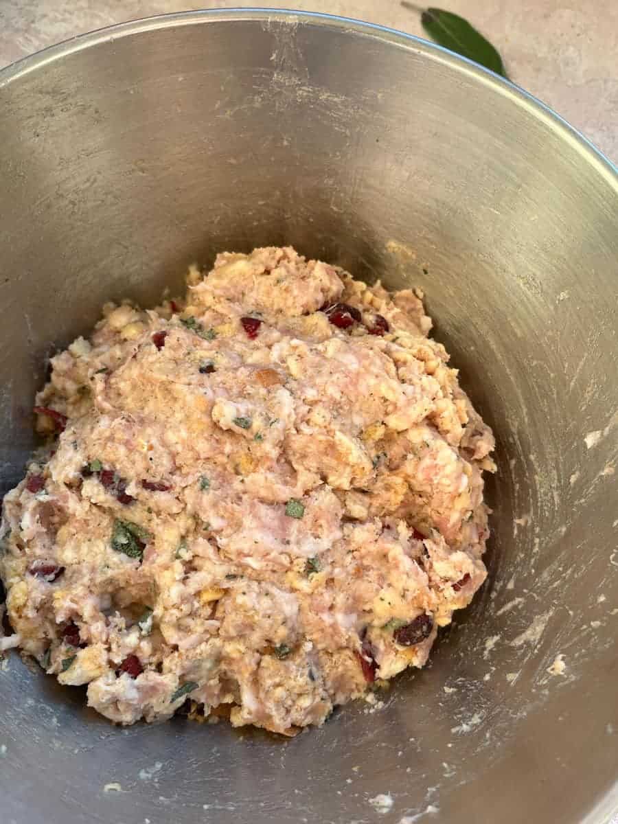 A silver bowl of sausage meat with dried cranberries and fresh chopped sage.