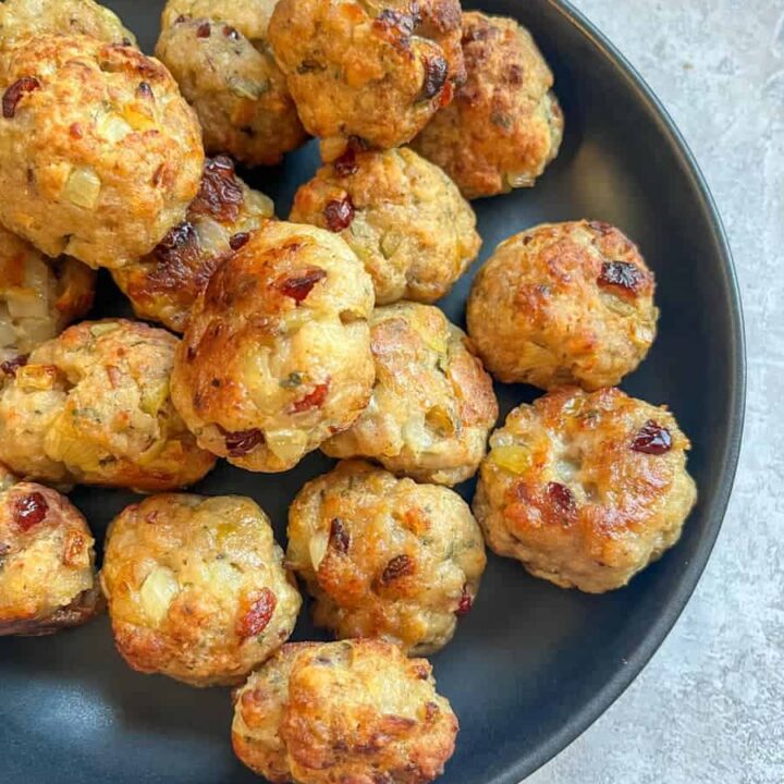A black dish of sausage stuffing balls with dried cranberries and chopped sage.