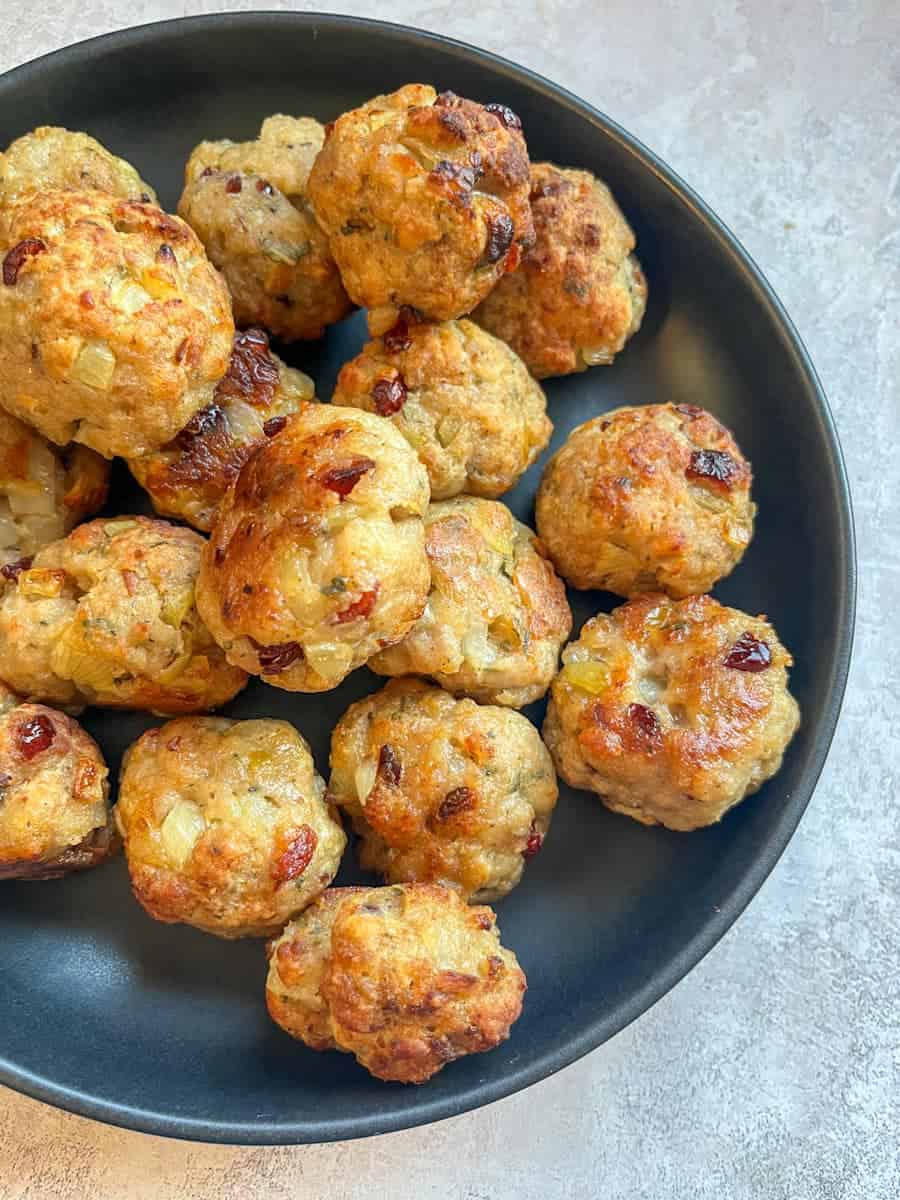 A black dish of sausage stuffing balls with dried cranberries and chopped sage.