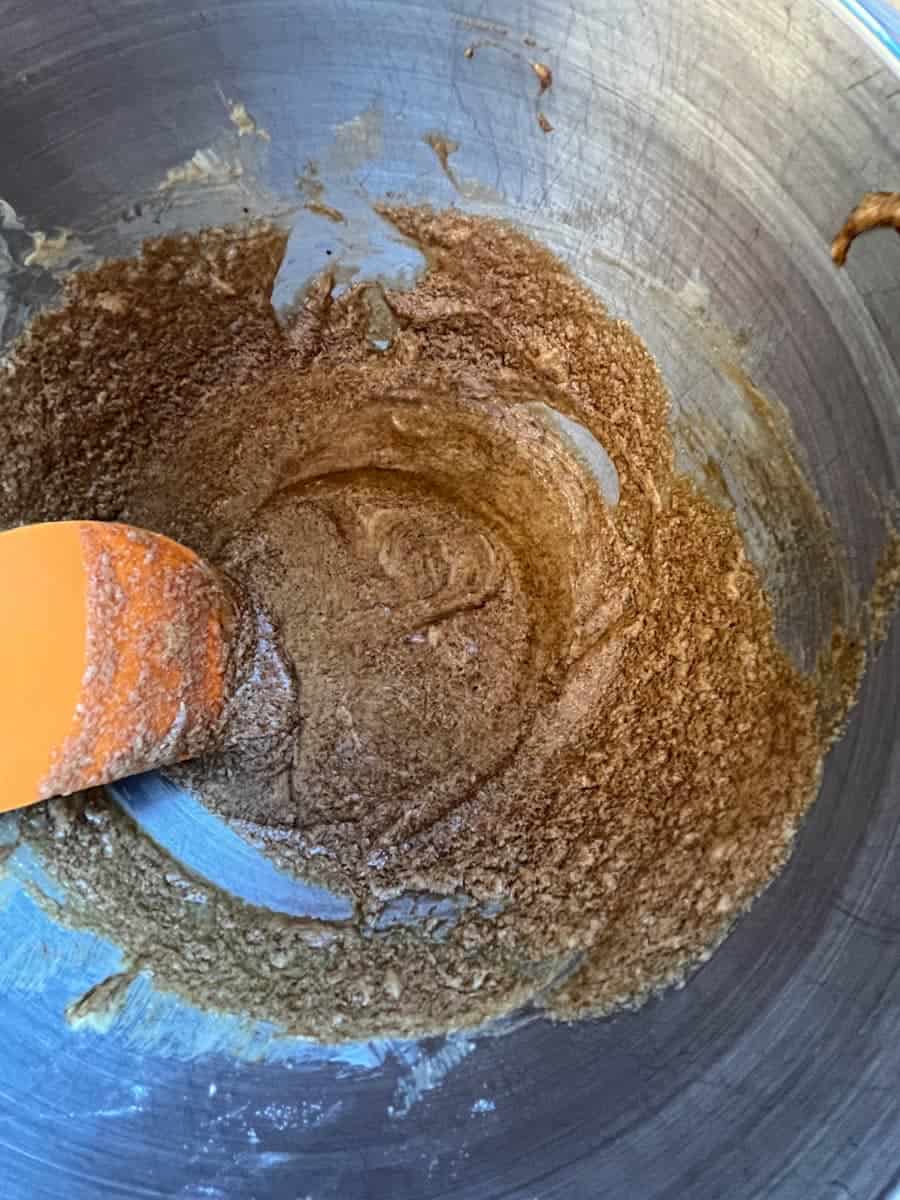 A mixture of eggs, brown sugar and butter in a silver bowl with an orange spatula.