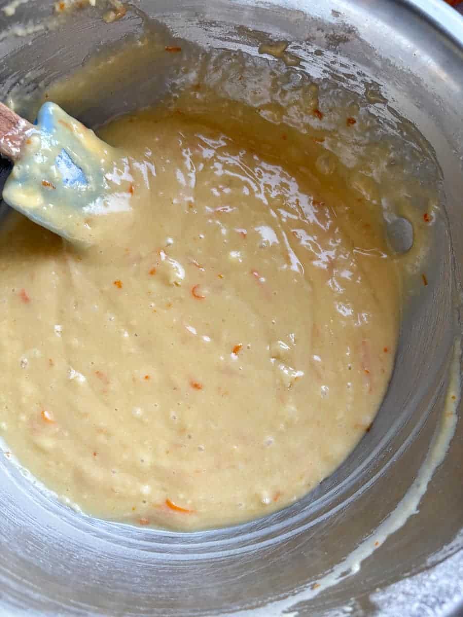 A silver bowl of orange cake batter with a blue spatula.