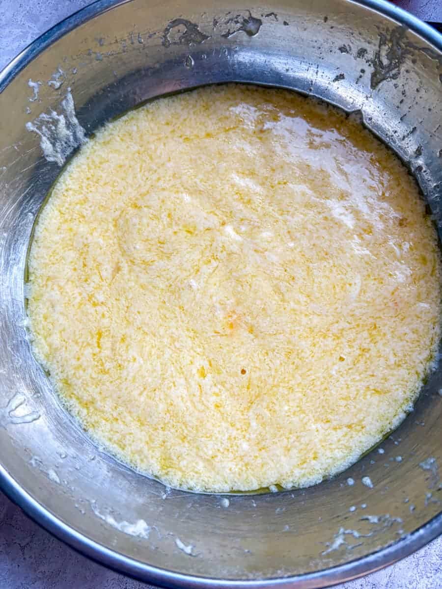 A silver bowl of beaten eggs, yoghurt and oil to make a cake.