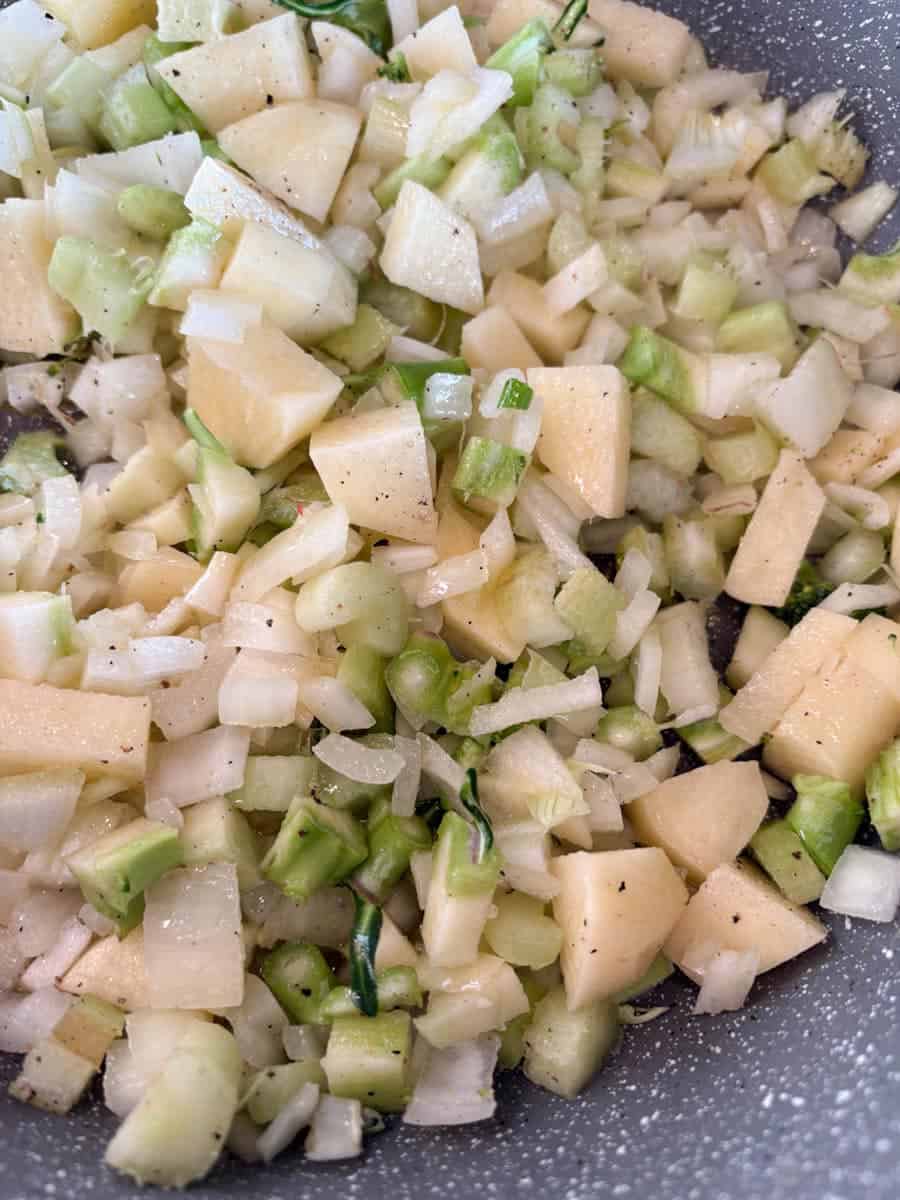Finely chopped potato, onion and celery in a grey pan.