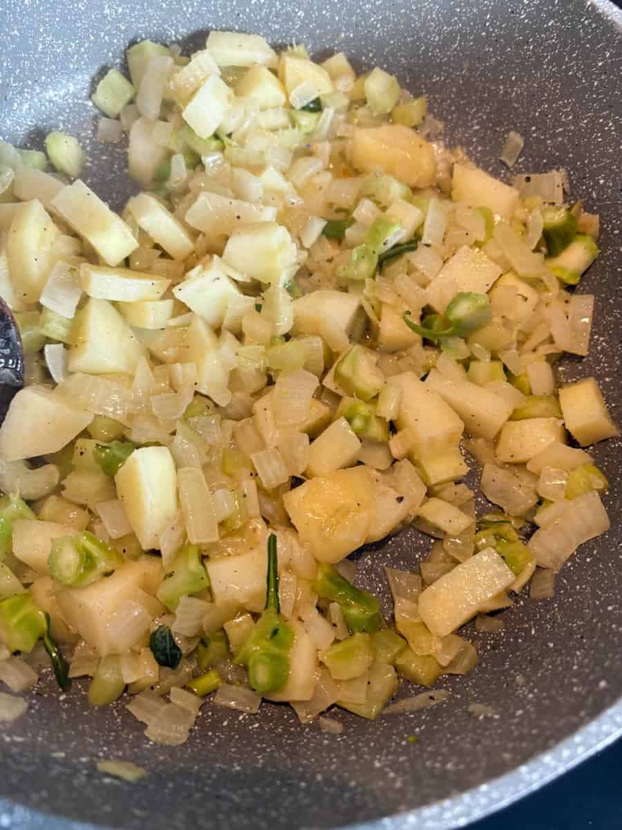 A grey pan with finely diced onion, celery and potato softening in butter and oil.