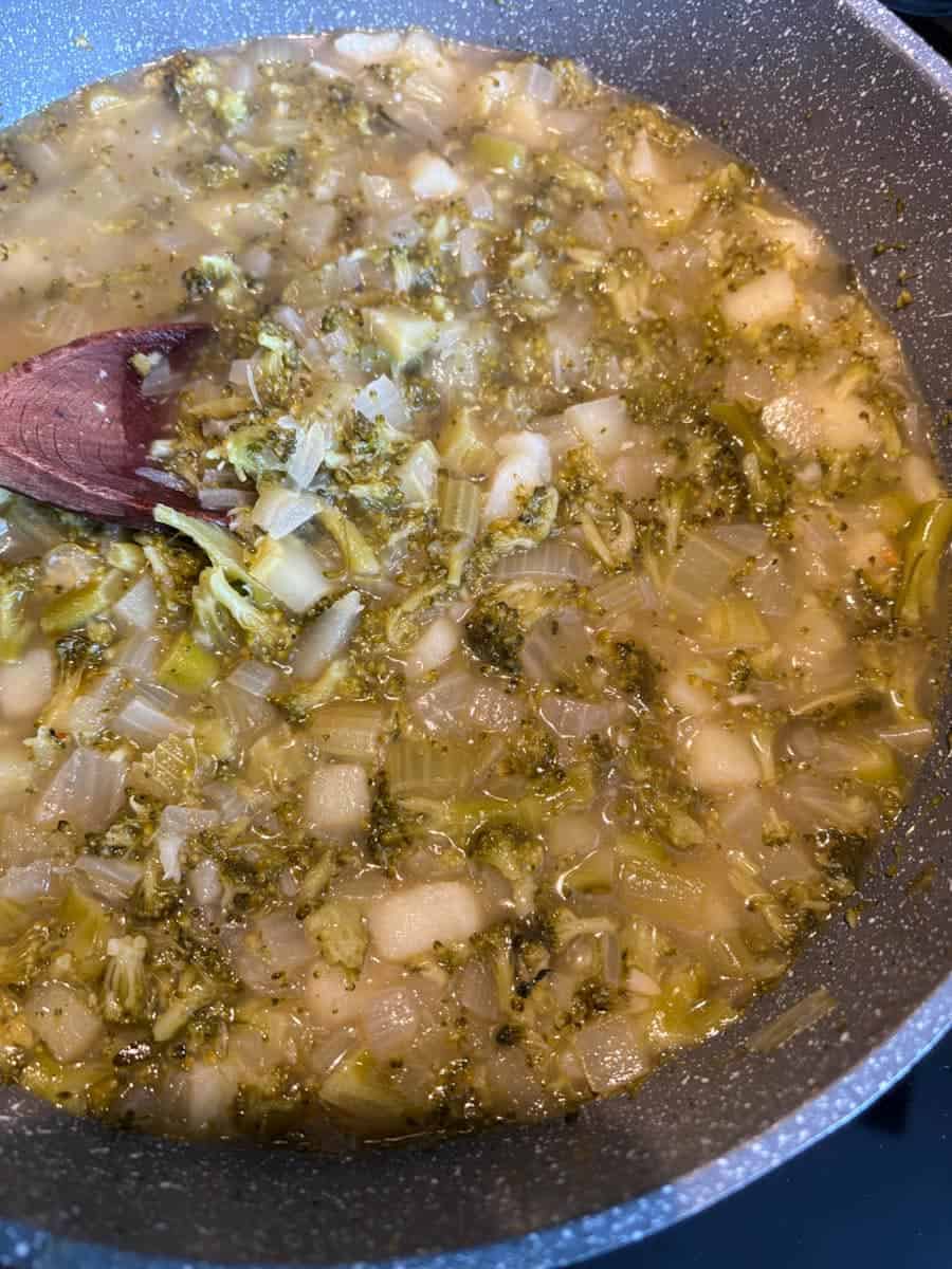A grey pan of cooked finely chopped broccoli, celery, onion and potato and stock.