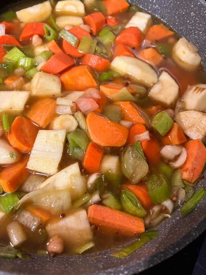 A grey pan of chopped parsnips, carrots, sweet potato, sliced leeks and chickpeas in vegetable stock.