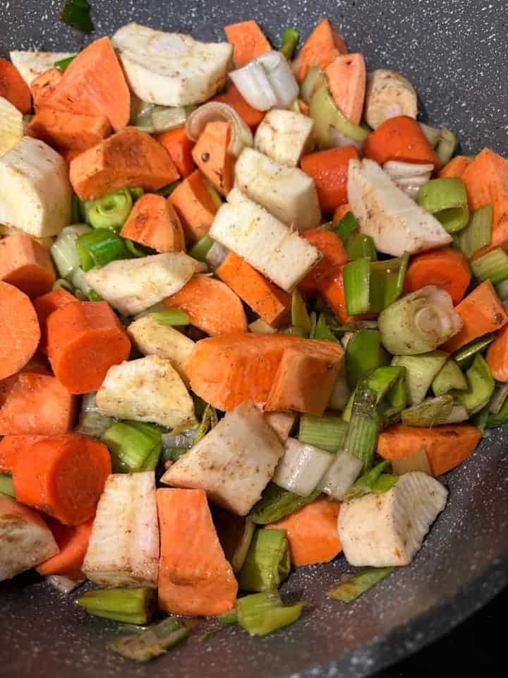 A grey pan with chopped leeks, diced sweet potato, parsnips and carrots.