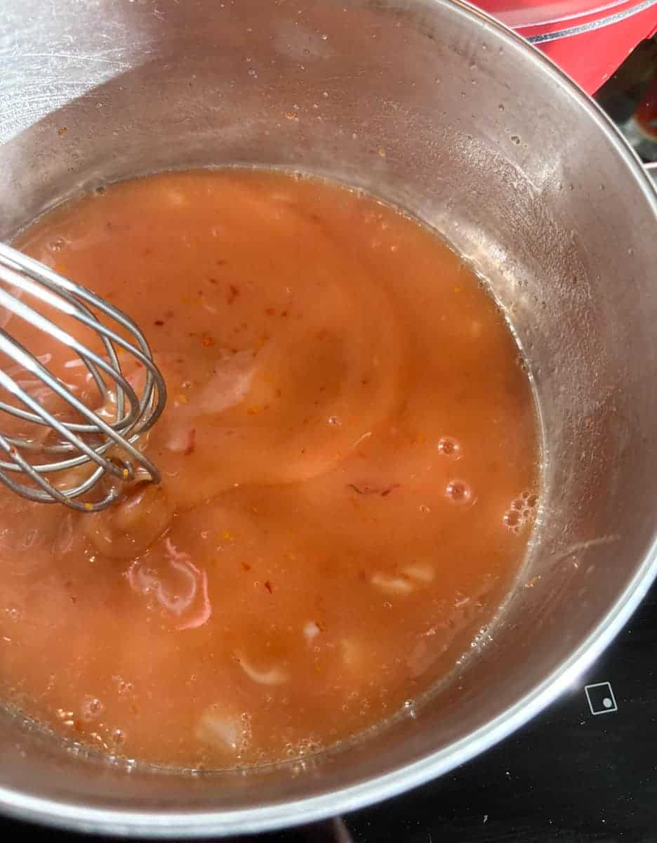 Blood orange curd being whisked in a silver saucepan.