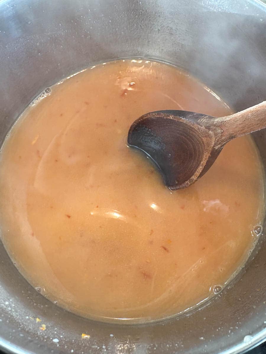 A silver saucepan of orange curd with a wooden spoon.
