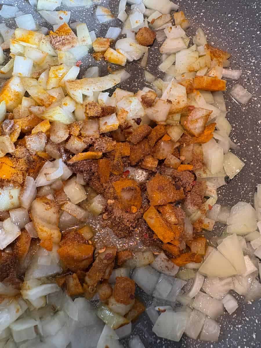 Chopped onions and spices cooking in a grey pan with coconut oil.