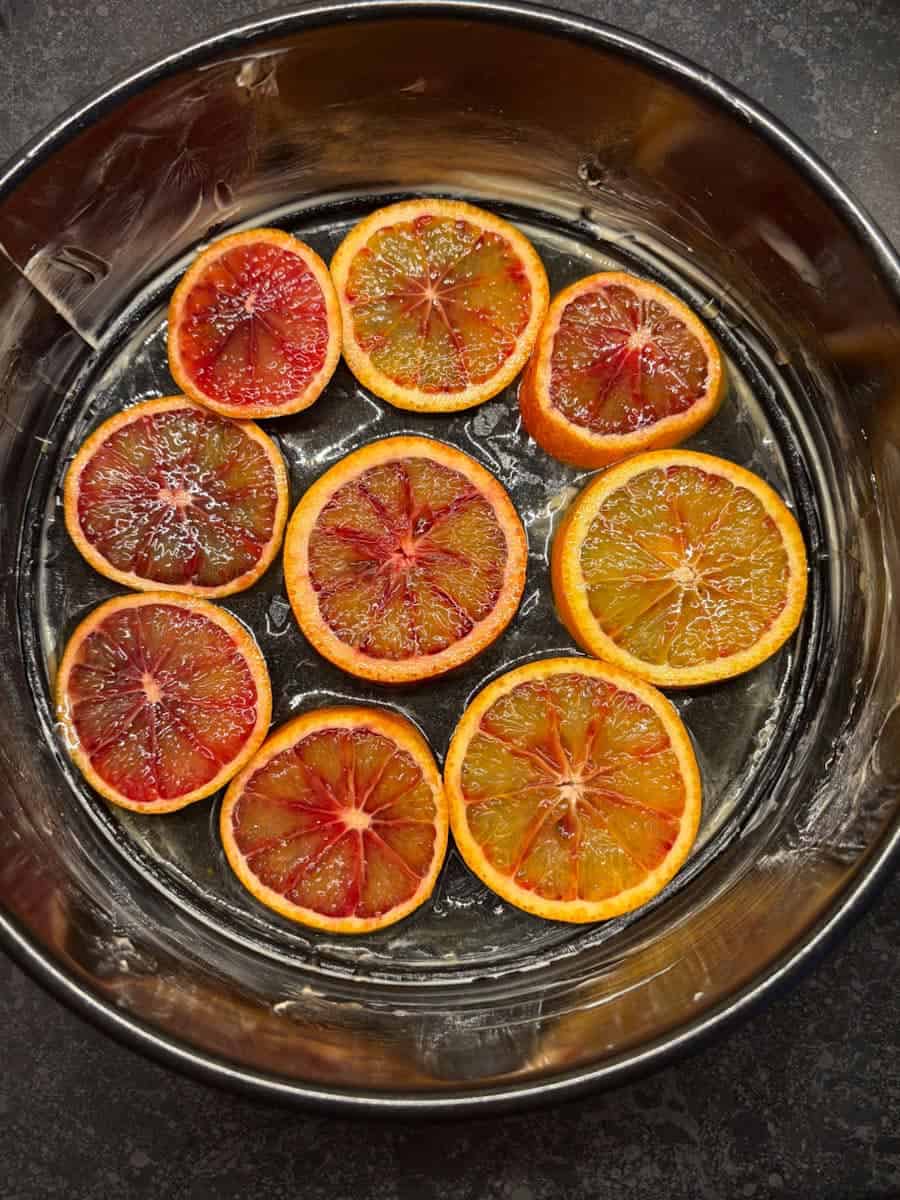 A round black cake tin greased with butter with sliced blood oranges at the base.