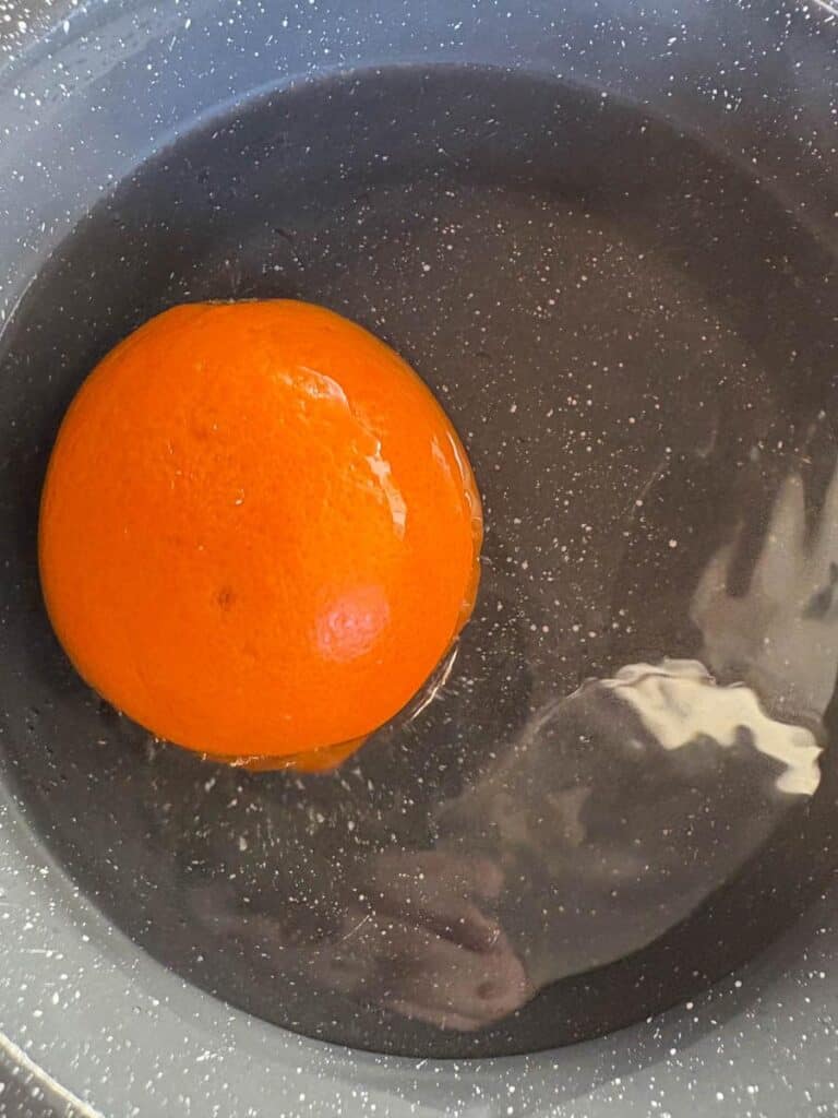 An orange in a grey saucepan filled with water.