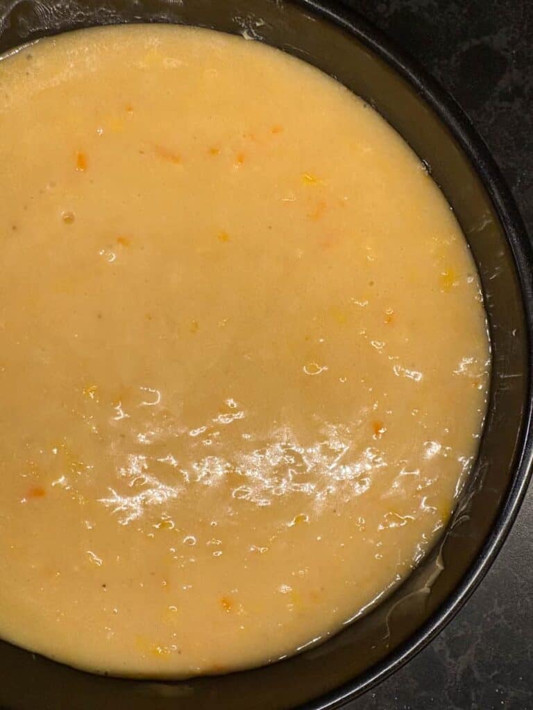 A black round cake tin filled with orange cake batter.