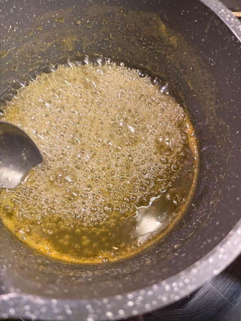 Orange syrup cooking in a grey saucepan with a silver spoon.