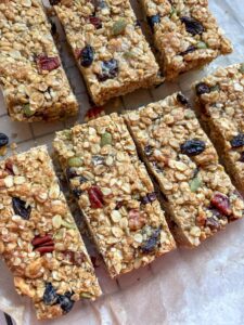 A batch of granola bars with mixed seeds, chopped nuts and dried fruit on a wire cooling rack lined with baking paper.