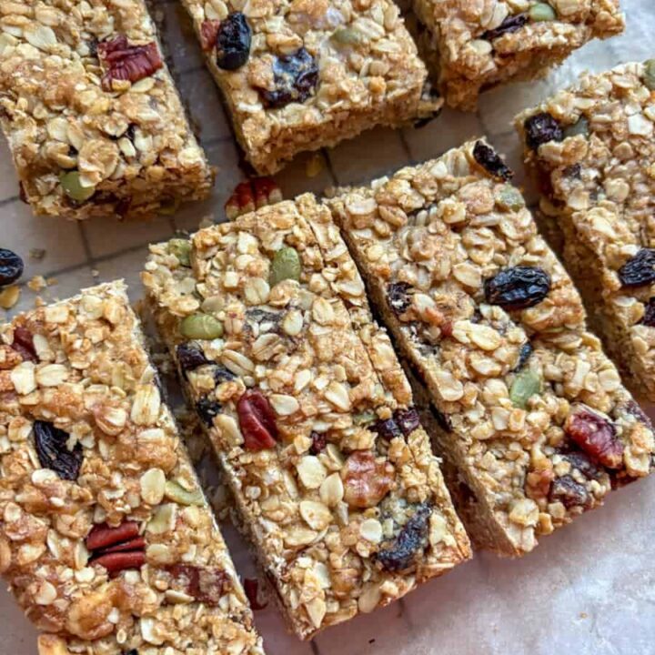A batch of granola bars with mixed seeds, chopped nuts and dried fruit on a wire cooling rack lined with baking paper.