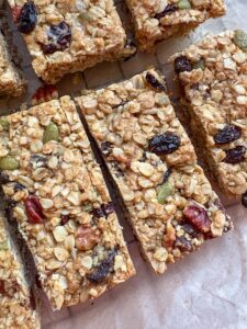 A batch of granola bars with dried fruit, chopped pecans and pumpkin seeds on a wire rack lined with baking paper.