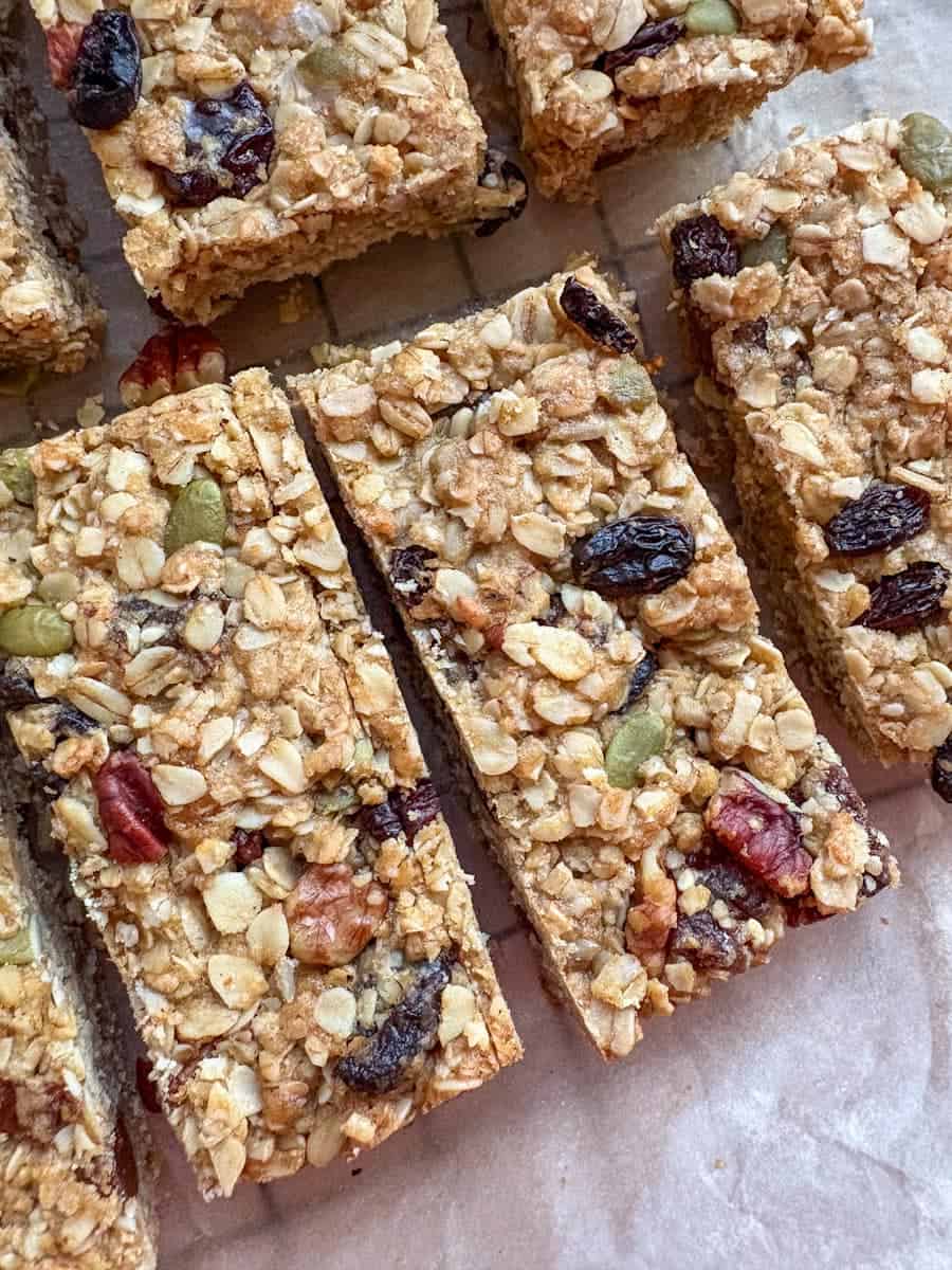 A batch of granola bars with dried fruit, chopped pecans and pumpkin seeds on a wire rack lined with baking paper.