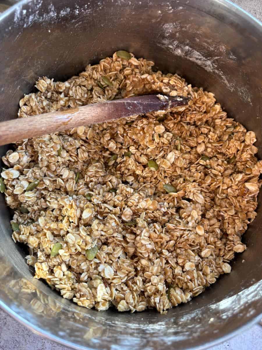 A large silver pan of oats, brown sugar and mixed seeds with a wooden spoon.