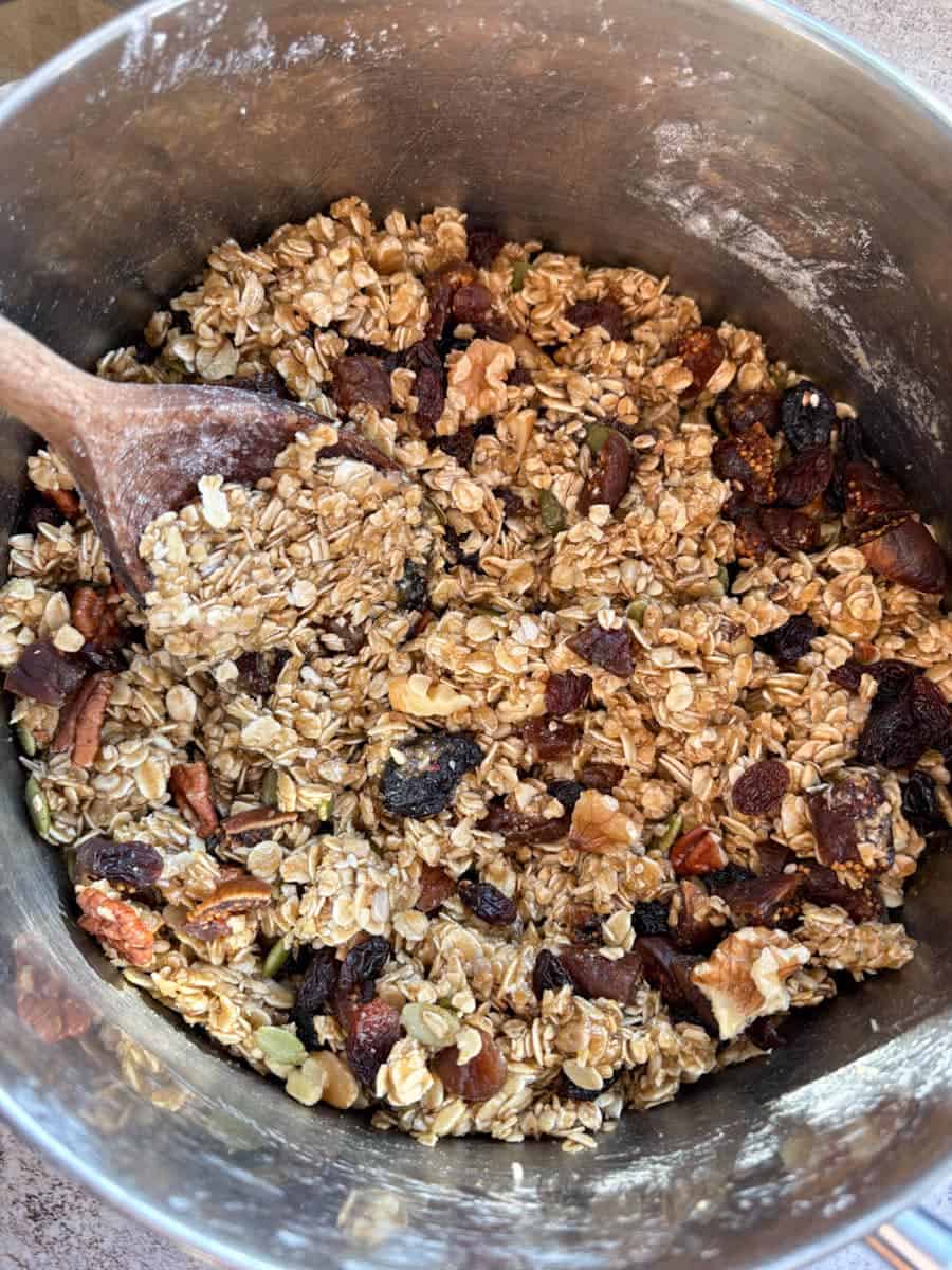 A large silver pan of oats, mixed seeds, dried fruit and chopped nuts mixed with melted butter.