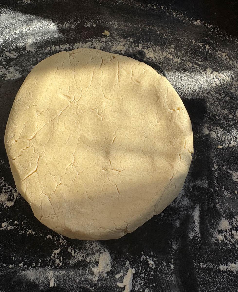 A piece of shortbread dough on a lightly floured dark grey kitchen counter.
