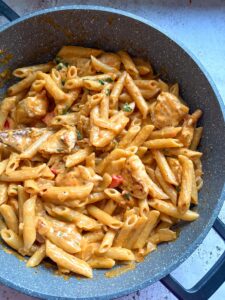 A grey pan of Peri Peri Chicken penne Pasta with diced onions and red peppers.