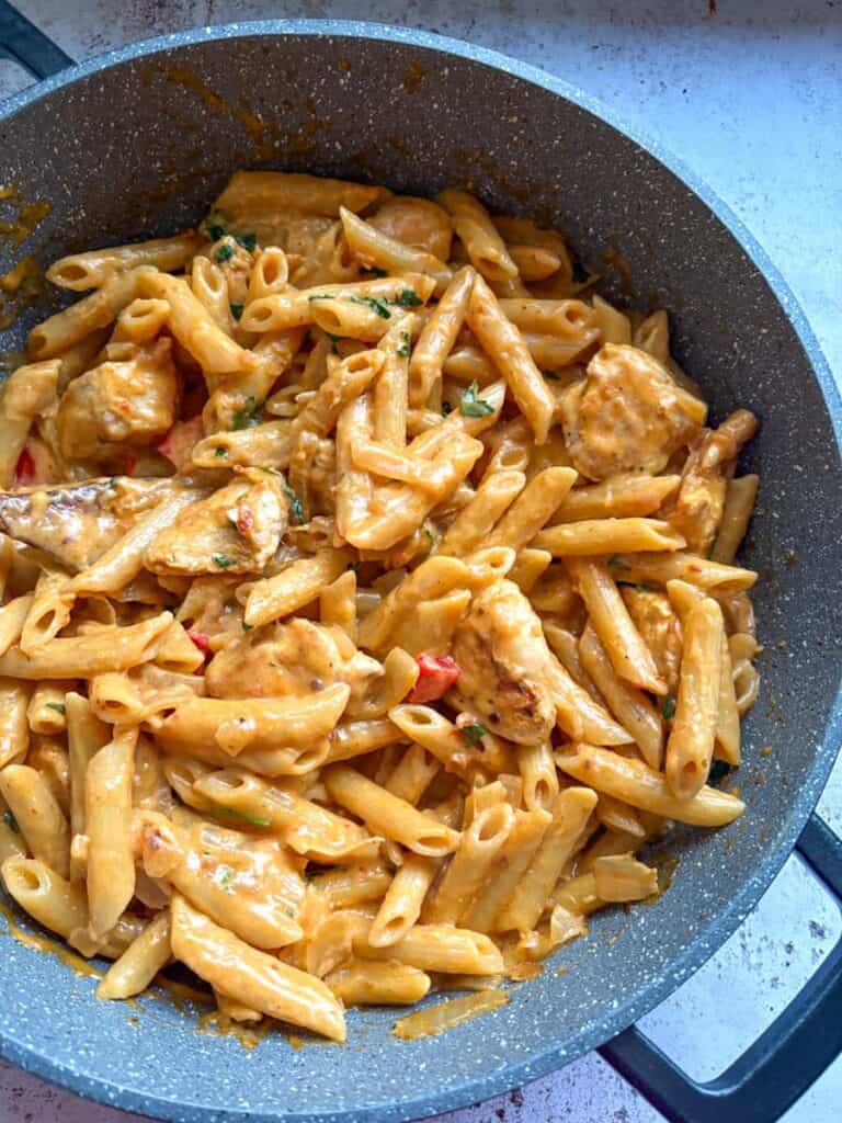 A grey pan of Peri Peri Chicken penne Pasta with diced onions and red peppers.