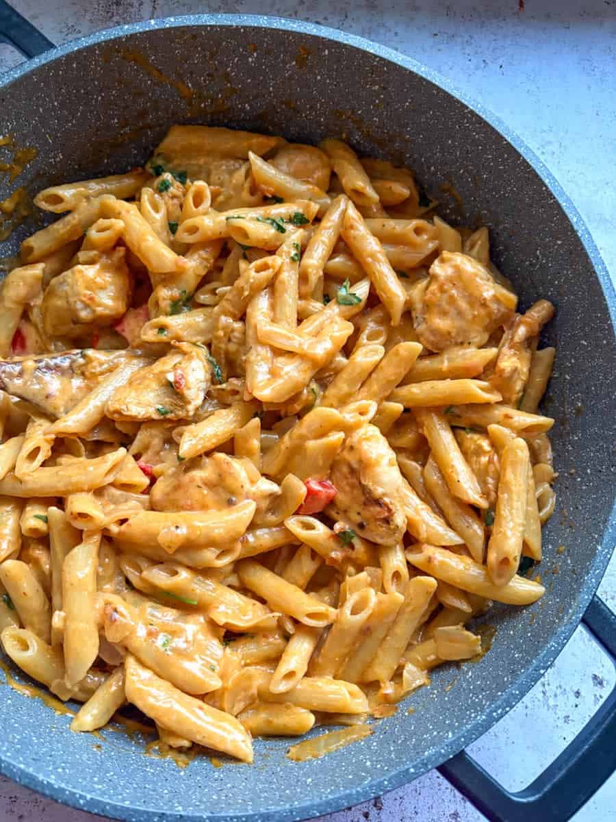 A grey pan of Peri Peri Chicken penne Pasta with diced onions and red peppers.