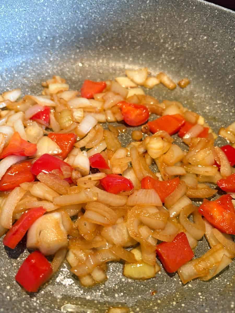 A grey pan of cooked diced onions and red peppers.