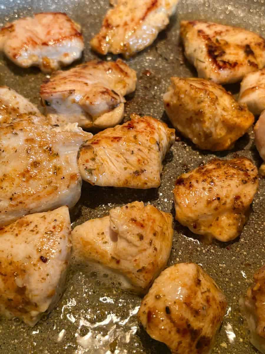 Chicken breast pieces coated in spices cooking in a grey pan.
