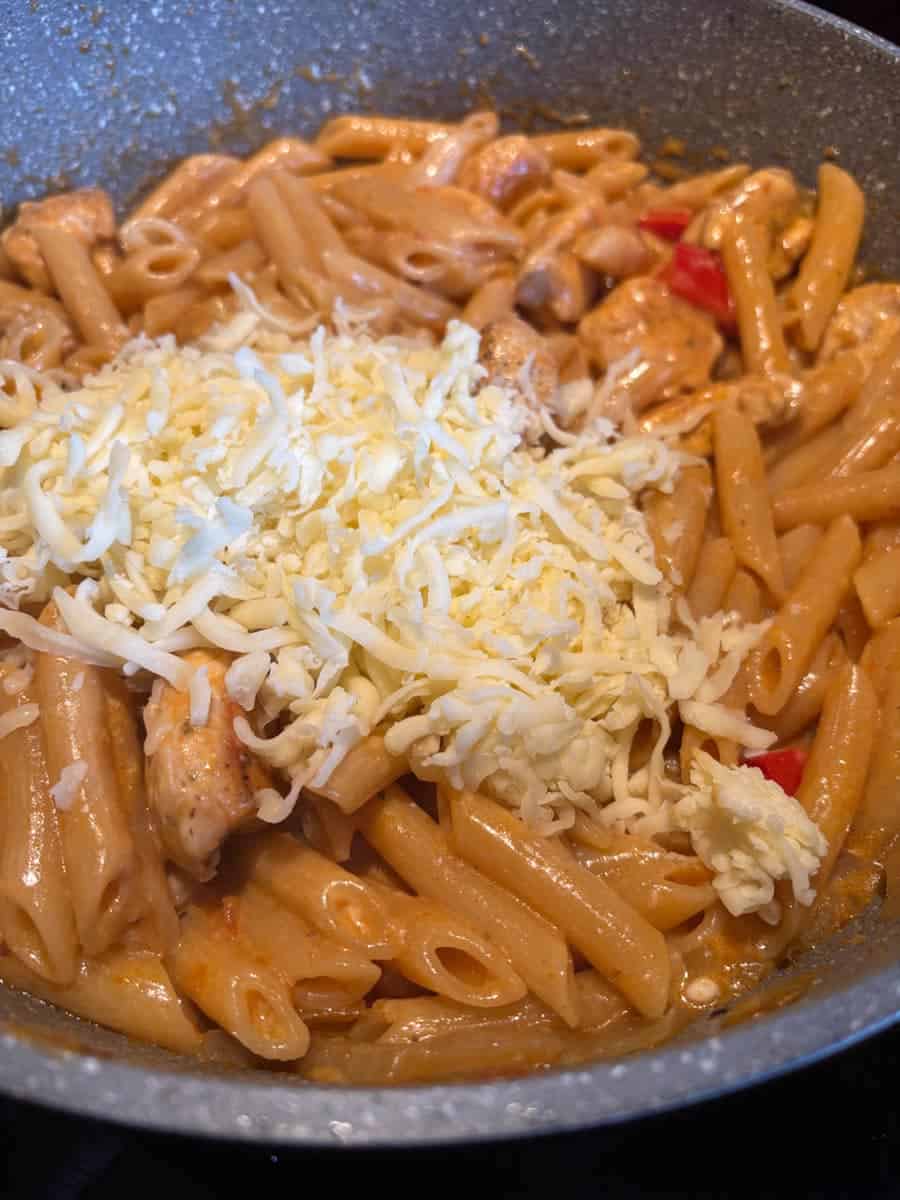 Grated Mozzarella cheese melting into a pan of Peri Peri chicken pasta.