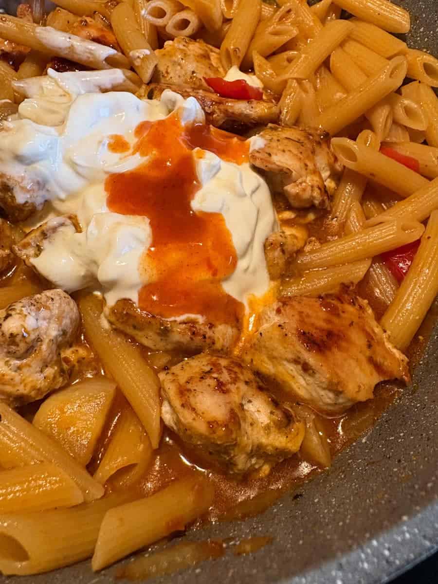 Peri Peri sauce and Greek yoghurt melting into a pan of pasta with spicy chicken, onions and peppers.