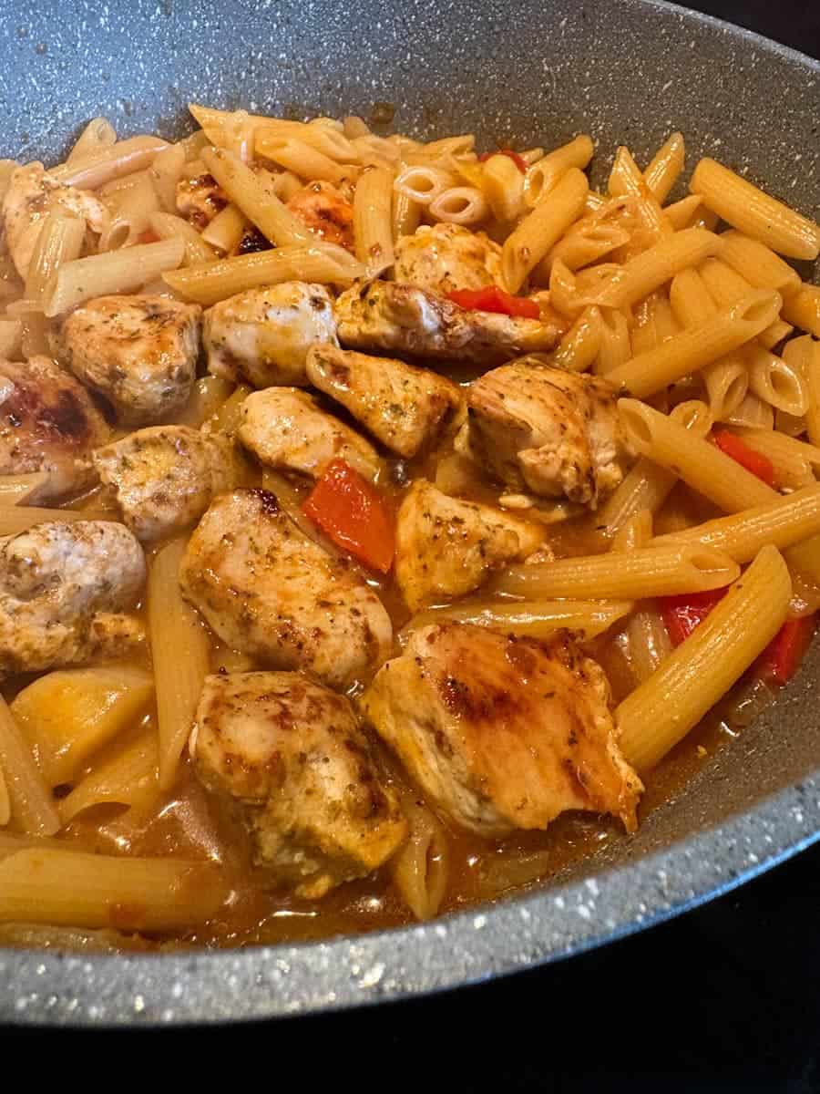 A pan of pasta with Peri Peri chicken, diced onion and red peppers.