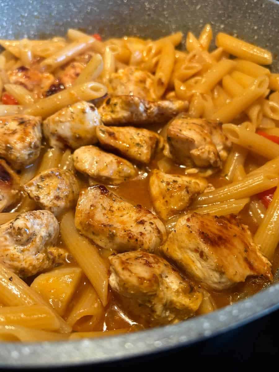 A grey saucepan of penne pasta with Peri Peri chicken and diced red peppers.