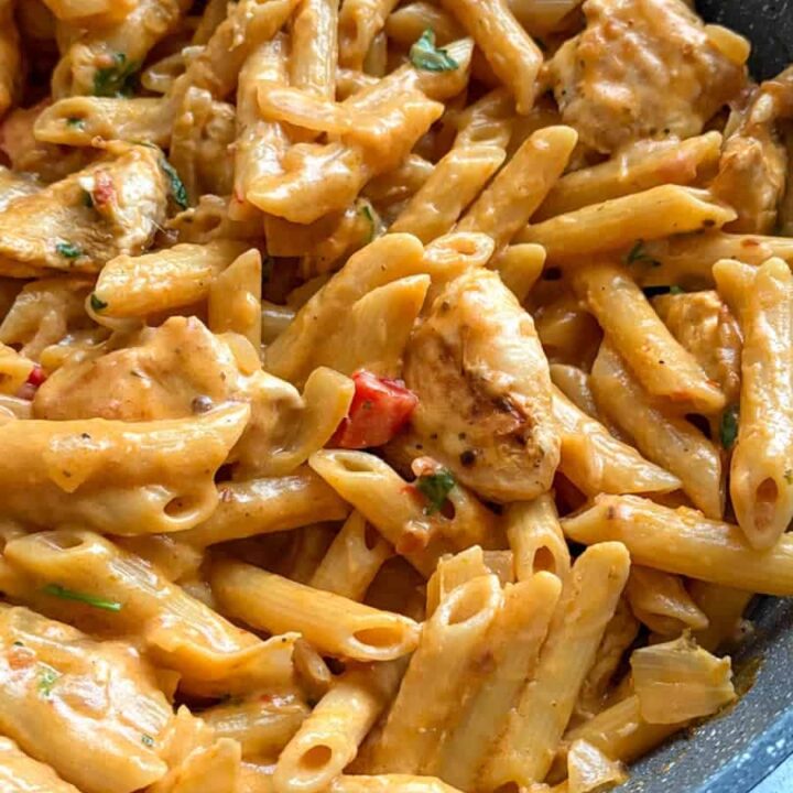 A pan of penne pasta with peri peri chicken, diced peppers and sliced onion in a creamy spiced sauce.