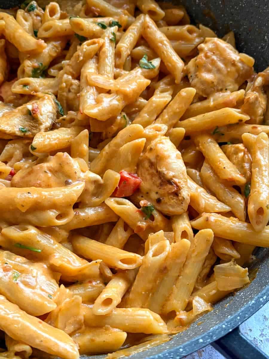 A pan of penne pasta with peri peri chicken, diced peppers and sliced onion in a creamy spiced sauce.